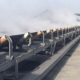 Bulk material conveyor belt supported by troughing rollers along the carrying run